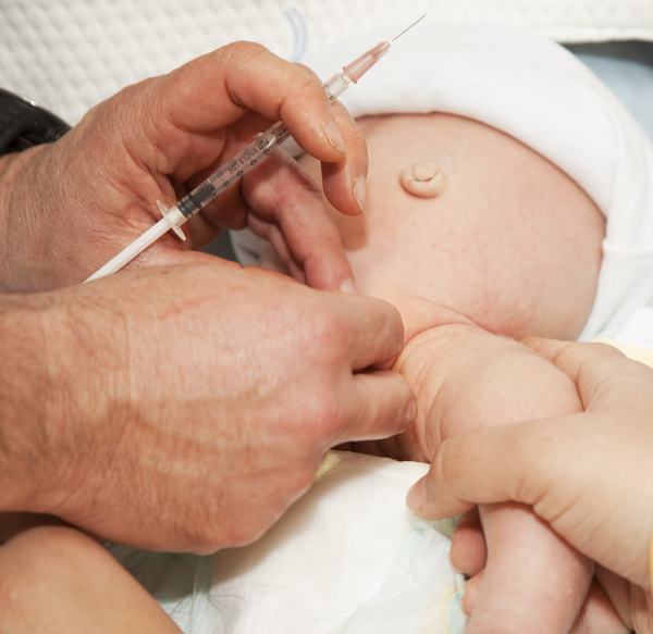 Doctor administering local anesthesia with a syringe to a newborn baby before a medical procedure.