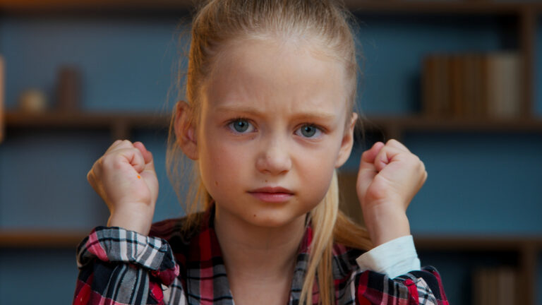Angry young girl frowning and clenching her fists, showing frustration or behavioral problems at home.
