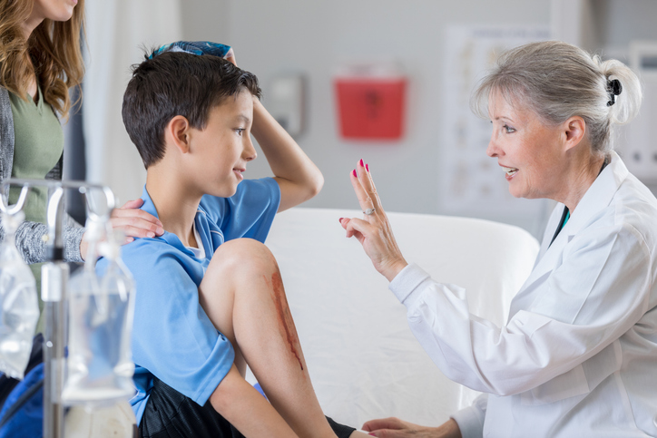 Doctor holding up fingers to test a young soccer player's vision for a concussion in a medical clinic.