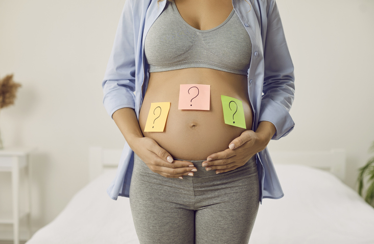 Close-up of a pregnant woman's belly with colorful sticky notes showing question marks, representing choice or uncertainty.